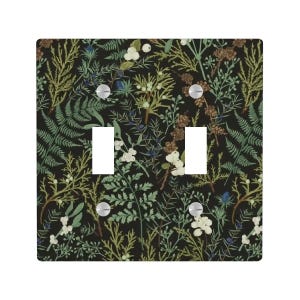 May include: A double light switch cover with a botanical design. The cover features a black background with a pattern of green ferns, white berries, and brown seed heads. The switch plate has two rectangular cutouts and silver screws.