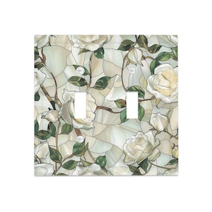 May include: A decorative light switch cover featuring a stained-glass design with white roses and green leaves. The cover has two switch openings and a pearlescent finish, adding a touch of elegance to any room.