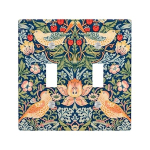 Puede incluir: Una cubierta decorativa para interruptor de luz doble con un patr&oacute;n repetido de p&aacute;jaros, flores y bayas en tonos naranja, rosa y verde sobre un fondo azul oscuro. La cubierta tiene dos aberturas para interruptores y tornillos plateados.