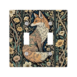 May include: A decorative double light switch cover featuring a detailed illustration of a fox with orange and cream fur, set against a dark background with floral and botanical patterns in yellow, blue, and green. The cover has two switch openings.