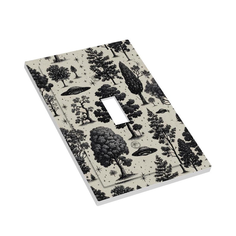 Op de afbeelding: Een lichtbeige enkele lichtschakelaar met een zwart-wit bos- en UFO-patroon. Het ontwerp toont verschillende boomsoorten, sterren en vliegende schotels. De schakelaaropening is rechthoekig.