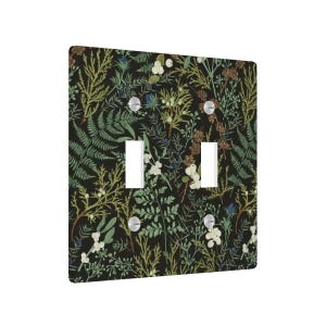 May include: A double light switch cover featuring a botanical design. The cover has a black background with a pattern of green, white, and brown plants. The switch openings are white, and the screws are silver.
