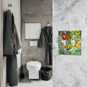 Puede incluir: Interior de ba&ntilde;o con una cubierta de interruptor de luz decorativa. La cubierta muestra un vibrante dise&ntilde;o floral con flores rojas, amarillas y azules. Dos albornoces grises cuelgan de ganchos. Un inodoro blanco y un cubo de basura negro tambi&eacute;n est&aacute;n presentes.