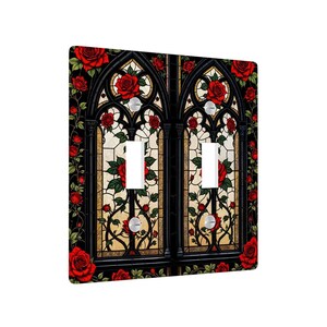 May include: A decorative double light switch cover featuring a stained-glass design. The design includes red roses, green leaves, and a black gothic arch pattern. The background is a light beige color.