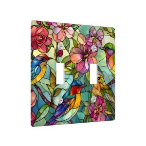 Puede incluir: Una cubierta decorativa para interruptor de luz con un dise&ntilde;o de vidriera colorido. La cubierta muestra p&aacute;jaros y flores vibrantes en tonos de azul, rojo, amarillo y rosa. El dise&ntilde;o incluye dos aberturas para interruptores de luz y est&aacute; montado con tornillos plateados.
