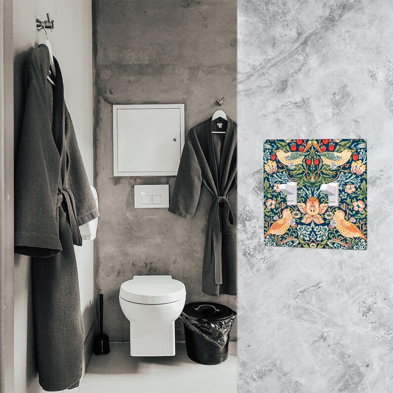 Puede incluir: Una cubierta decorativa para interruptor de luz doble con un dise&ntilde;o floral y de p&aacute;jaros. La cubierta presenta un fondo azul oscuro con p&aacute;jaros amarillos, bayas rojas y hojas verdes. La cubierta del interruptor est&aacute; montada en una pared de m&aacute;rmol gris.