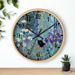 Puede incluir: Un reloj de pared redondo con marco de madera clara. La esfera del reloj presenta un diseño floral con iris, margaritas y un gato negro. Los números negros marcan las horas. Las manecillas del reloj son negras.