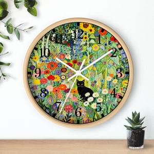 Puede incluir: Reloj de pared redondo con marco de madera clara. La esfera presenta un diseño floral colorido con un gato negro. Los números negros marcan las horas. Las manecillas blancas indican la hora.