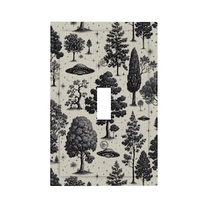 Op de afbeelding: Een lichtschakelaarcover met een zwart-wit illustratie van bomen, sterren en UFO's op een beige achtergrond. Het heeft een opening voor een enkele tuimelschakelaar.