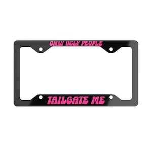 Puede incluir: Un marco de matrícula negro rectangular con el texto ONLY UGLY PEOPLE impreso en una fuente rosa ondulada en la barra superior y el texto TAILGATE ME en la misma fuente en la barra inferior, con cuatro orificios de montaje.