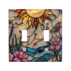 May include: A decorative light switch cover featuring a stained glass design. The artwork depicts a sun, butterfly, and flowers in shades of orange, yellow, blue, and pink. The cover has two switch openings and silver screws.