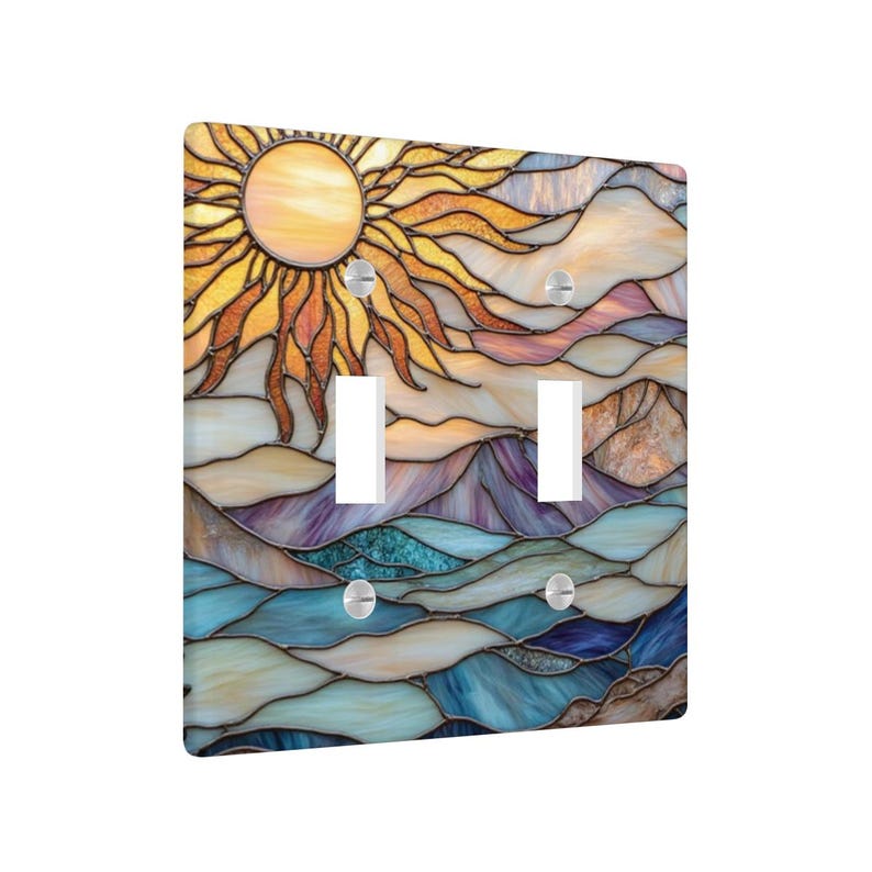 May include: A decorative double light switch cover with a stained glass design. The artwork shows a sun in yellow and orange, above a landscape of blue, purple, and beige. The cover has two switch openings and silver screws.