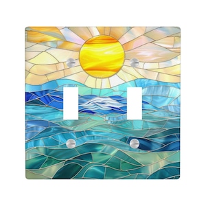 Puede incluir: Una cubierta de interruptor de luz doble decorativa con un diseño de vidriera. La obra de arte representa un sol amarillo brillante sobre una escena de océano azul y verde. El diseño está formado por muchas formas pequeñas e irregulares.