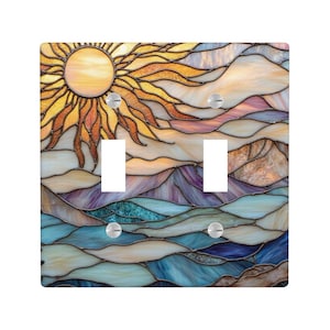 May include: A decorative double light switch cover with a stained glass design. The artwork shows a sun with yellow and orange rays, above a landscape of mountains and water in shades of blue, purple, and beige.