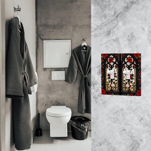May include: A decorative double light switch cover featuring a stained glass design with red roses and green leaves. The design is set against a black background with white light switches. The cover is mounted on a gray marble wall.