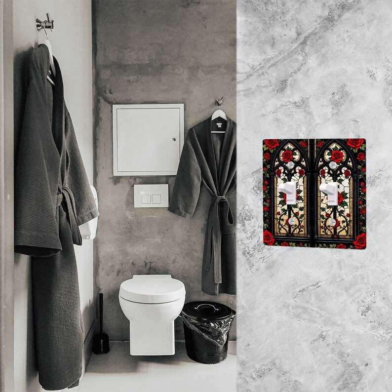May include: A decorative double light switch cover featuring a stained glass design with red roses and green leaves. The design is set against a black background with white light switches. The cover is mounted on a gray marble wall.