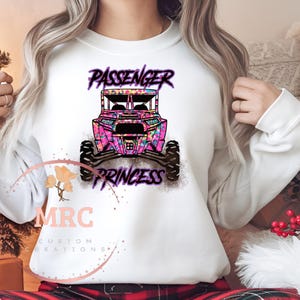 May include: White sweatshirt with a pink and purple design of an off-road vehicle with the text "Passenger Princess" on it.