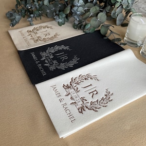 May include: Three white linen napkins with a brown monogram and the text "J/R 25.09.23" and "JAMES & RACHEL". One napkin is black with a silver monogram.