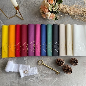 May include: A set of 12 place cards featuring a gold circle and monogram design. The place cards are in a variety of colours, including yellow, orange, red, burgundy, purple, pink, blue, green, grey, black, white and cream.