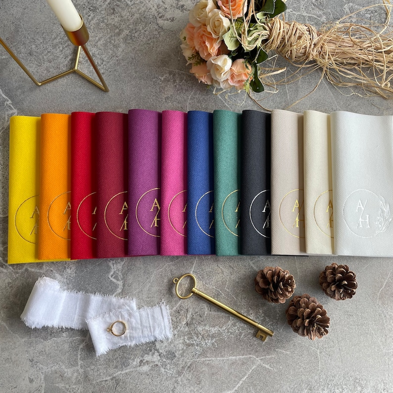 May include: A set of 12 place cards featuring a gold circle and monogram design. The place cards are in a variety of colours, including yellow, orange, red, burgundy, purple, pink, blue, green, grey, black, white and cream.