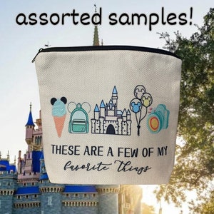 May include: A beige canvas zippered pouch with a black zipper. The pouch has an embroidered design of a castle, Mickey Mouse ears, a backpack, an ice cream cone, and a camera. The text "These are a few of my favorite things" is embroidered on the pouch.