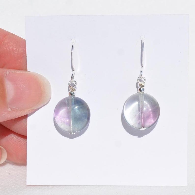 May include: Dangle earrings with spherical, translucent beads in shades of purple, blue, and clear. The earrings have silver-coloured hooks and small accent beads. The earrings are displayed against a white background.