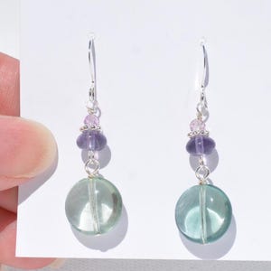 May include: Dangle earrings with a large, round, translucent green bead at the base, with a smaller purple bead and pink beads above. The earrings have silver-coloured hooks.