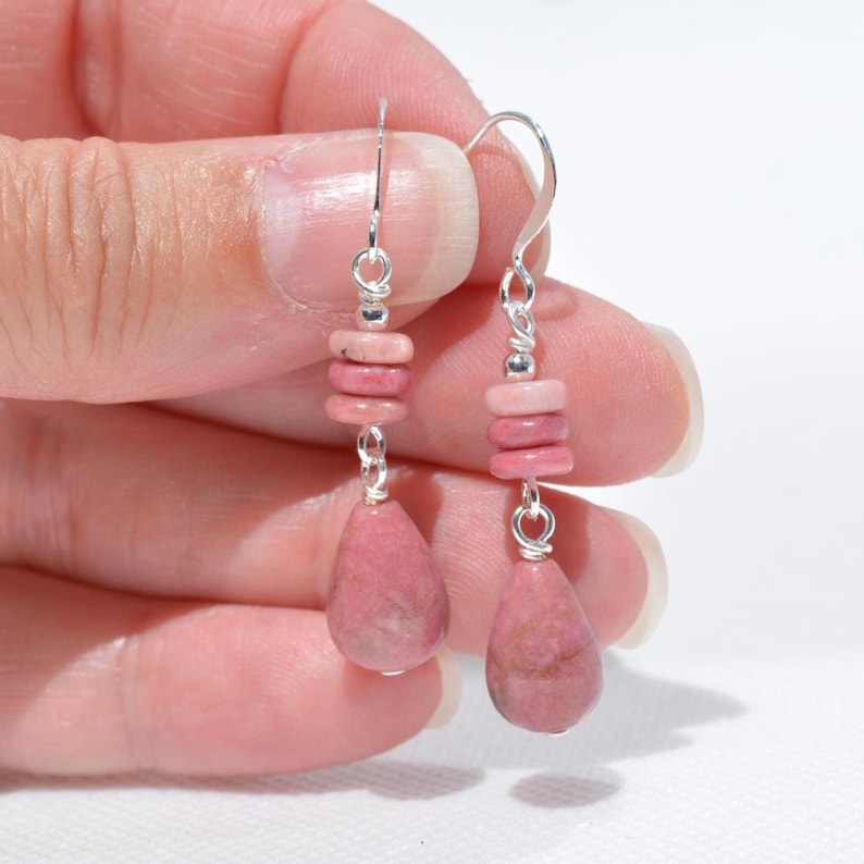 Peut inclure: Une paire de boucles d'oreilles pendantes avec des crochets argent&eacute;s, chacune orn&eacute;e de deux petits disques en pierre rose empil&eacute;s et d'un pendentif en pierre rose en forme de goutte, lisse et plus grand, suspendu par une fine cha&icirc;ne argent&eacute;e.