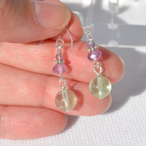 May include: Dangle earrings with silver hooks and wire. Each earring features a light green, round bead at the bottom, with a pink gemstone and smaller beads above. The earrings are held up by a silver hook.