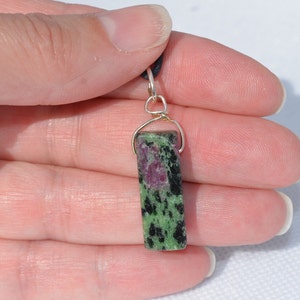 May include: A green and pink gemstone pendant with black flecks, set in a silver wire wrap.