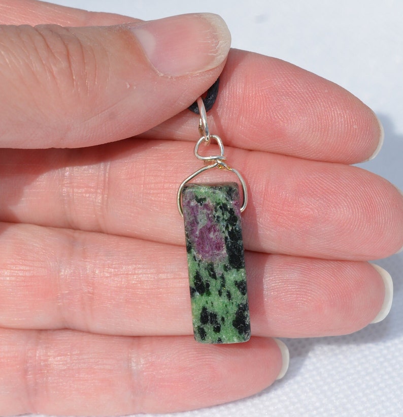 May include: A green and pink gemstone pendant with black flecks, set in a silver wire wrap.
