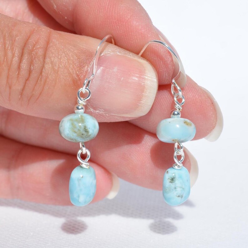 May include: A pair of dangle earrings featuring light blue and green gemstone beads. The earrings have a silver-colored hook and connecting wires. The gemstones are oval and oblong in shape.