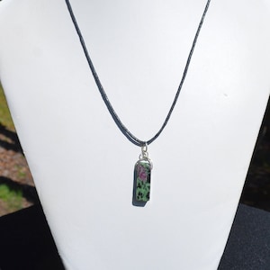 May include: A black cord necklace with a green and pink stone pendant. The stone is rectangular and has a silver bail.