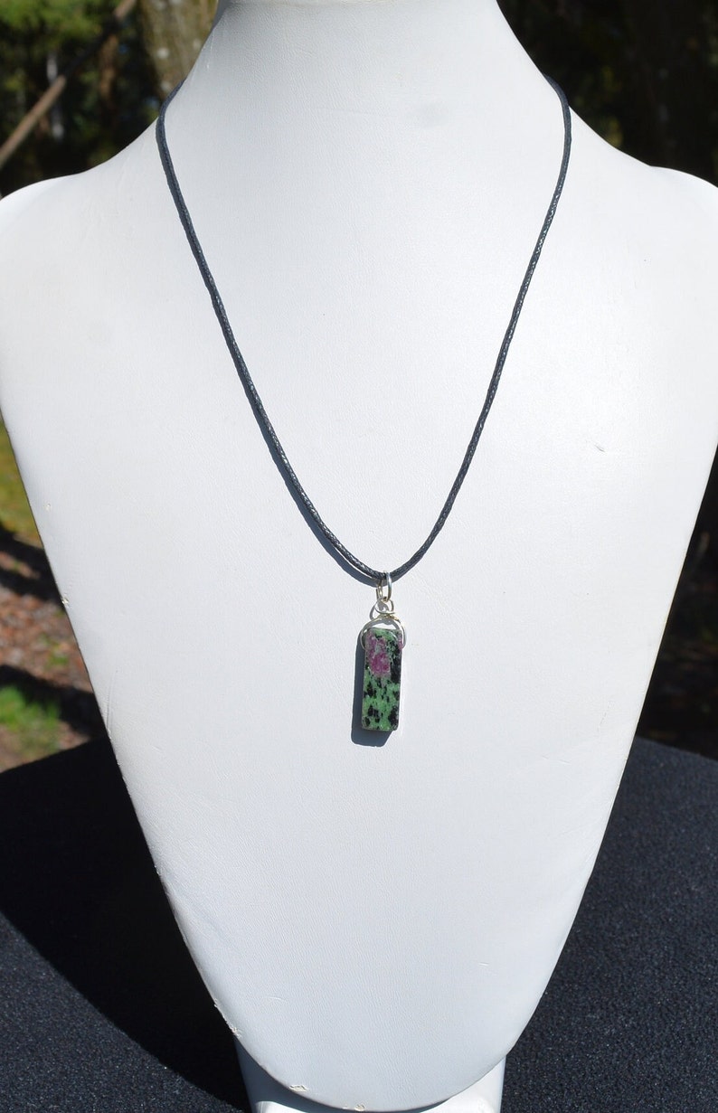 May include: A black cord necklace with a green and pink stone pendant. The stone is rectangular and has a silver bail.