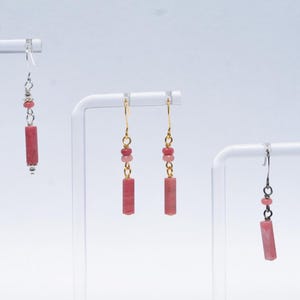 May include: Three pairs of drop earrings featuring cylindrical pink stone beads suspended from metal hooks. Each earring includes small round accent beads above the central cylinder. The metal hardware varies in tone between silver and gold finishes.