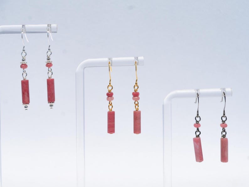 May include: Three pairs of drop earrings featuring cylindrical pink stone beads suspended from metal hooks. Each earring includes small round accent beads above the central cylinder. The metal hardware varies in tone between silver and gold finishes.