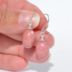 Peut inclure: Une paire de boucles d'oreilles pendantes avec des pierres pr&eacute;cieuses en rhodochrosite rose de forme ovale et lisse. Chaque pierre est suspendue &agrave; un crochet en m&eacute;tal argent&eacute; et orn&eacute;e d'une petite coupelle d&eacute;corative argent&eacute;e sur le dessus.