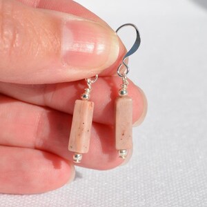 May include: A pair of drop earrings featuring rectangular, light peach-coloured stone beads. Each bead is accented with small, polished silver-toned metal beads at the top and bottom, suspended from simple silver-toned metal ear wire hooks.