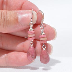 Peut inclure: Une paire de boucles d'oreilles pendantes avec des crochets argent&eacute;s et des attaches en fil m&eacute;tallique. Chaque boucle pr&eacute;sente trois petites perles rondes en pierre rose empil&eacute;es, surmontant un pendentif en pierre rose en forme de goutte.