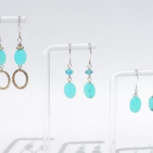 May include: Three pairs of drop earrings featuring bright turquoise oval beads and silver-toned hardware. The first pair includes textured silver rings, the second pair features smaller turquoise beads above larger ones, and the third pair has single turquoise beads.