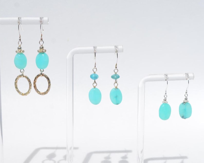May include: Three pairs of drop earrings featuring bright turquoise oval beads and silver-toned hardware. The first pair includes textured silver rings, the second pair features smaller turquoise beads above larger ones, and the third pair has single turquoise beads.