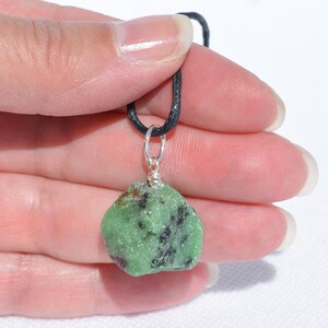 May include: A green and black gemstone pendant on a black cord. The pendant is attached to a silver bail.