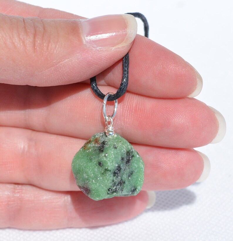 May include: A green and black gemstone pendant on a black cord. The pendant is attached to a silver bail.