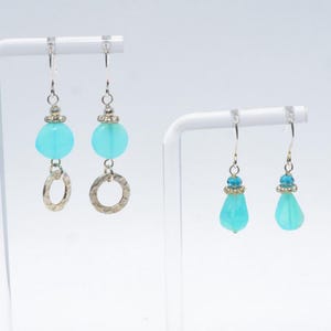 May include: Two pairs of dangle earrings featuring turquoise-coloured beads. The first pair has round beads and hammered silver-tone rings. The second pair features smaller faceted blue beads and smooth, teardrop-shaped turquoise-coloured beads.