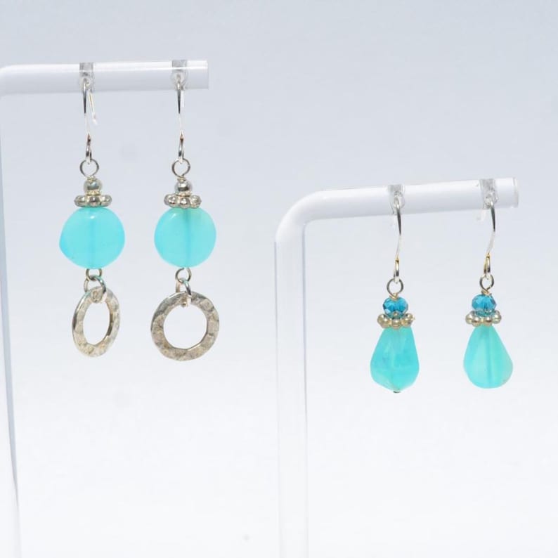 May include: Two pairs of dangle earrings featuring turquoise-coloured beads. The first pair has round beads and hammered silver-tone rings. The second pair features smaller faceted blue beads and smooth, teardrop-shaped turquoise-coloured beads.
