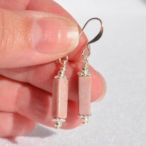 May include: A pair of drop earrings featuring cylindrical, dusty pink stone beads. Each bead is accented with small, textured silver-toned metal caps at the top and bottom, suspended from simple silver-toned metal ear wires for a clean look.
