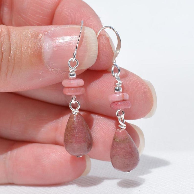Peut inclure: Une paire de boucles d'oreilles pendantes avec des crochets argent&eacute;s et des attaches en fil m&eacute;tallique. Chaque boucle se compose de deux petites perles en pierre rose, plates et circulaires, surmontant un pendentif en pierre rose en forme de goutte.