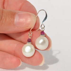 May include: A pair of silver dangle earrings with white pearl drops and pink gemstone accents.
