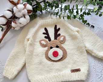 May include: A cream-colored knitted sweater with a brown and white reindeer applique. The reindeer has a red nose and brown antlers.