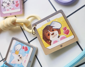 May include: Wooden dog-themed keychains with colorful illustrations. Each keychain features a different dog breed, a hand, and hearts. The keychains are attached to various colored cords and a yellow ring.